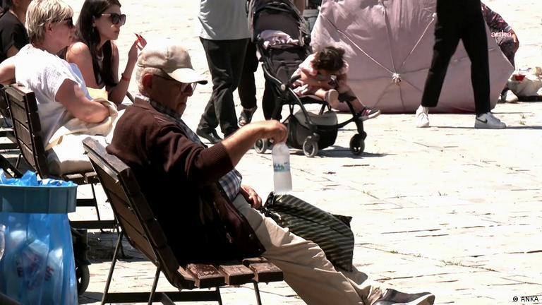 Emekli olduğu tahmin edilen yaşlı bir adam sokakta bir bankta elinde su şişesi ile oturuyor 