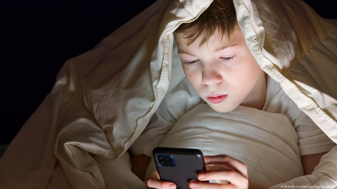 Un niño mira su teléfono inteligente debajo de una sábana. Un niño mira su teléfono inteligente debajo de una sábana.