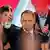 A man in a dark suit and red tie with a badge in the colours of the Polish flag on his lapel (Karol Nawrocki) makes the victory sign with his right hand, Warsaw, Poland, June 1, 2025. Two people are clapping behind him. Other people are making the victory sign in the foreground