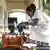 Picture of a smiling woman dressed in white pouring a drink into cups.