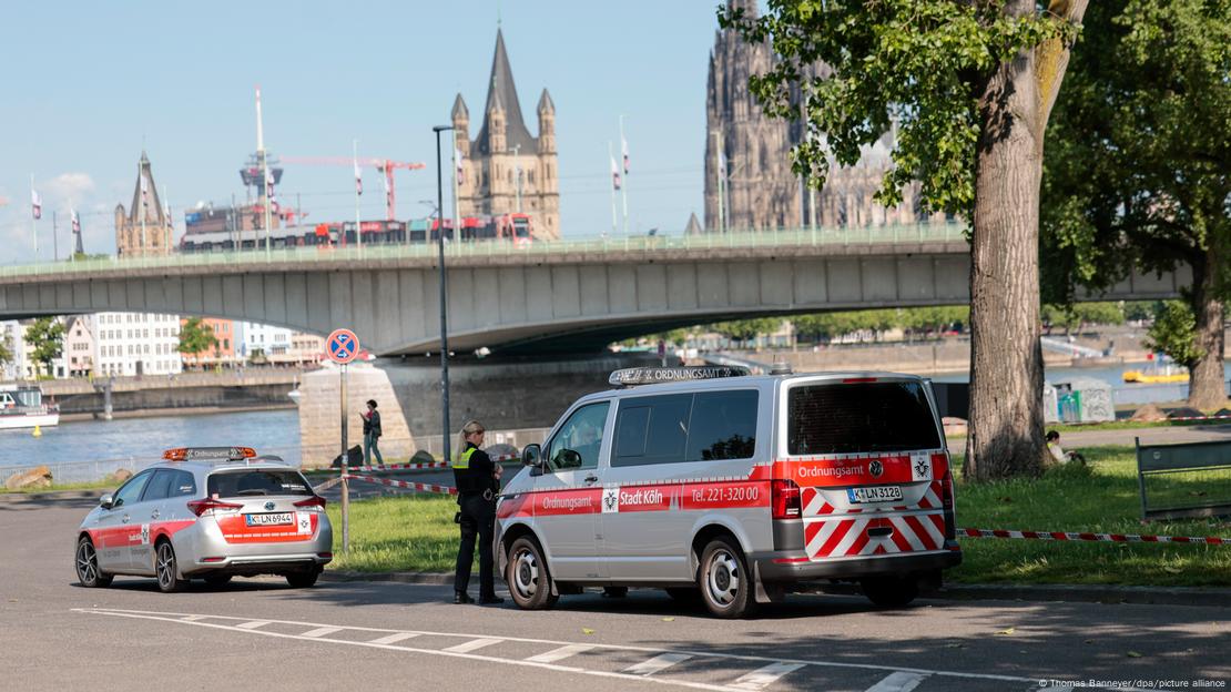 Vehículos de la oficina de orden público están estacionados en la orilla derecha del Rin, frente al puente Deutzer. Al fondo, se ve la Gran Iglesia de San Martín junto a la Catedral de Colonia y, a lo lejos, se alza la torre de televisión.