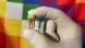 A gloved hand holding an ancient tooth extracted from an old skeleton, in front of a multi-colored flag A gloved hand holding an ancient tooth extracted from an old skeleton, in front of a multi-colored flag