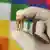 A gloved hand holding an ancient tooth extracted from an old skeleton, in front of a multi-colored flag
