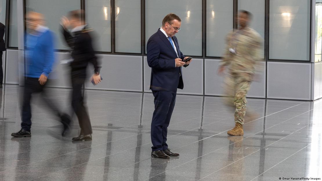 Beim NATO-Verteidigungsministertreffen in Brüssel schaut Verteidigungsminister Boris Pistorius auf sein Handy, links und rechts von ihm sind unscharf mehrere Personen zu sehen