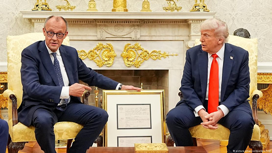 Bundeskanzler Friedrich Merz überreicht US-Präsident Donald Trump Geburtsurkunde seines Großvaters im Oval Office, beide sitzen auf Stühlen nebeneinander 