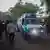 An ambulance passes by a crowd of onlookers on a tree-lined street