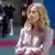 A woman in a pale lilac suit and blonde hair (Italian Prime Minister Giorgia Meloni) looks upward as a military band can be made out behind her in a photo taken on May 17,2025