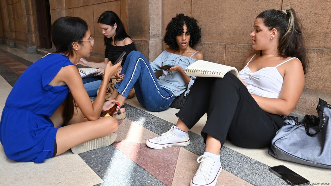 Estudiantes de la Universidad de La Habana sentadas en el suelo con sus apuntes y sus teléfonos móviles. Estudiantes de la Universidad de La Habana sentadas en el suelo con sus apuntes y sus teléfonos móviles.