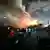 Israel Rehovot 2025 | Rettungspersonal an einem Wohngebäude nach iranischem Raketenangriff in Zentralisrael, aus dem hinteren Teil der Ruine schlagen Flammen
