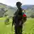 Disidente de las FARC apostado con uniforme, bandera colombiana como brazalete y arma.