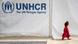 Ein kleines Mädchen in einem roten Kleid geht an einem Zelt mit der Aufschrift "UNHCR The UN Refugee Agency" vorbei. Ein kleines Mädchen in einem roten Kleid geht an einem Zelt mit der Aufschrift "UNHCR The UN Refugee Agency" vorbei.