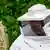 A man in white protective gear confronts a nest of Asian hornets