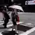 A woman walks over a road with a sun umbrella