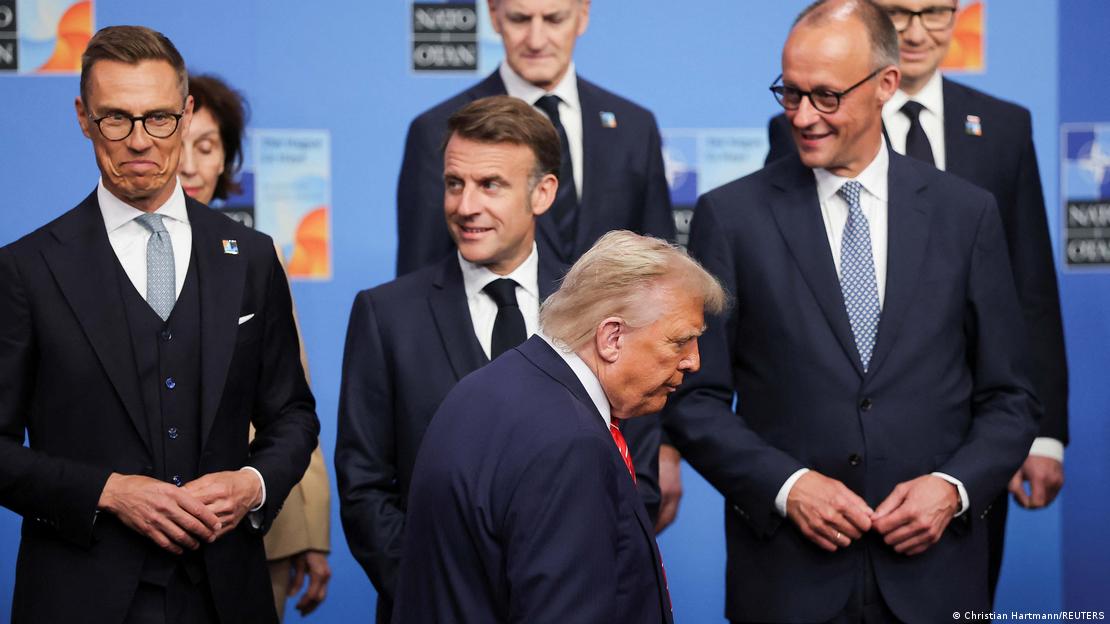 Donald Trump geht zu seinem Platz beim Gruppenfoto, hinter ihm Alexander Stubb, der das Gesicht verzieht, Emmanuel Macron und Friedrich Merz