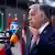 Ein Mann in einem blauen Anzug (Viktor Orban) steht vor Mikrofonen von Fernsehteams und spricht, während er mit der rechten Hand gestikuliert