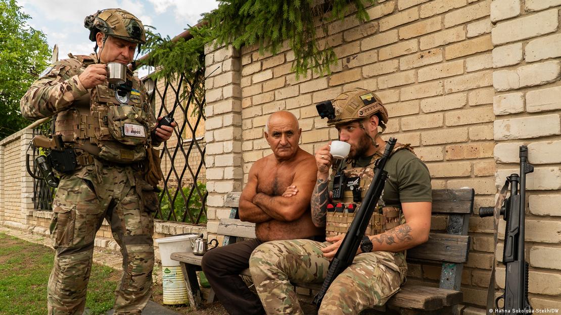 Поліцейські евакуаційної групи "Білий янгол" Геннадій (ліворуч) і Дмитро (праворуч) пʼють чай в компанії місцевого мешканця Валерія, Костянтинівка, Донецька область, червень 2025 року