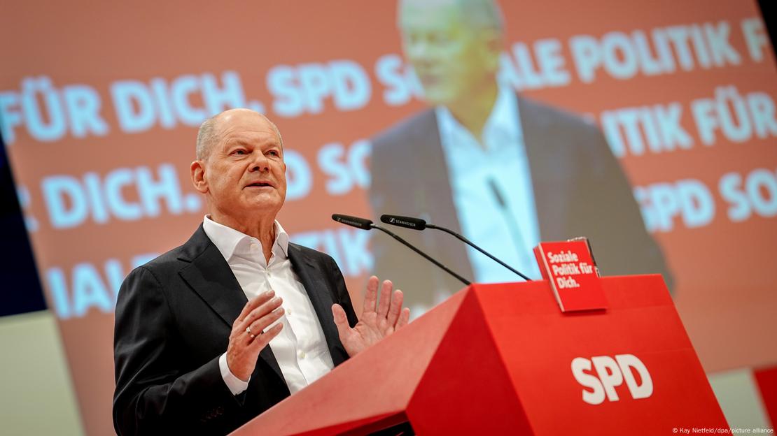 Olaf Scholz flet në Kongresin e SPD me duart ngritur, pas ti një monitor Olaf Scholz flet në Kongresin e SPD me duart ngritur, pas ti një monitor