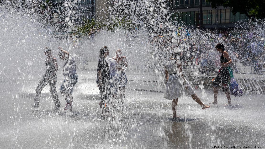 Am Karlsplatz in München, der Landeshauptstadt des Bundeslandes Bayern, erfrischen sich Passanten an einem Brunnen 