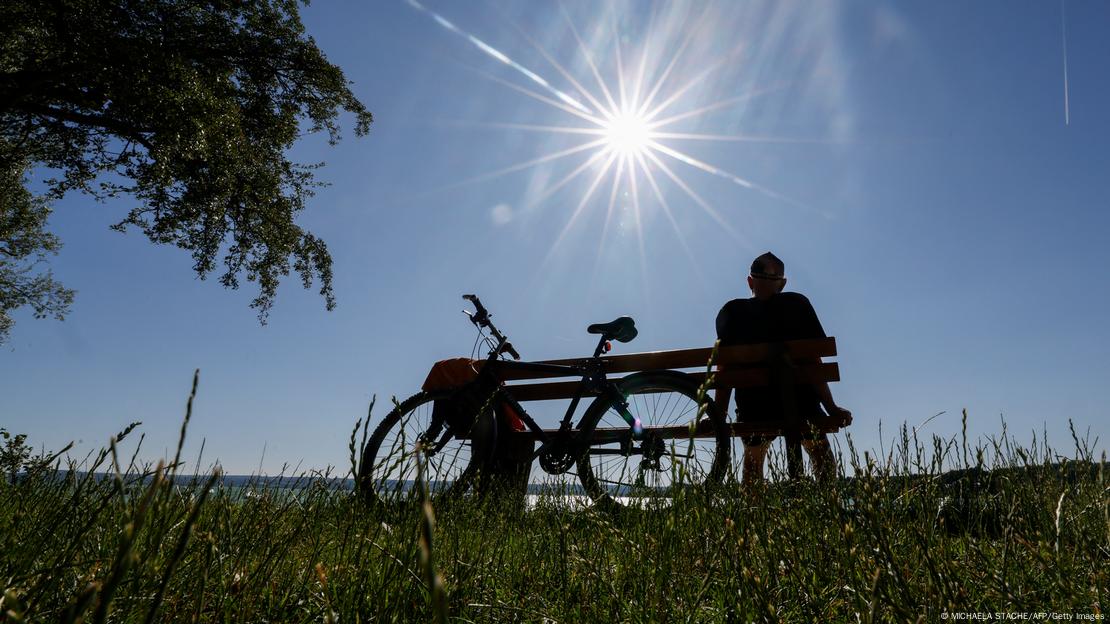 Homem sentado em banco ao lado de sua bicicleta nas margens do lago Ammersee Homem sentado em banco ao lado de sua bicicleta nas margens do lago Ammersee
