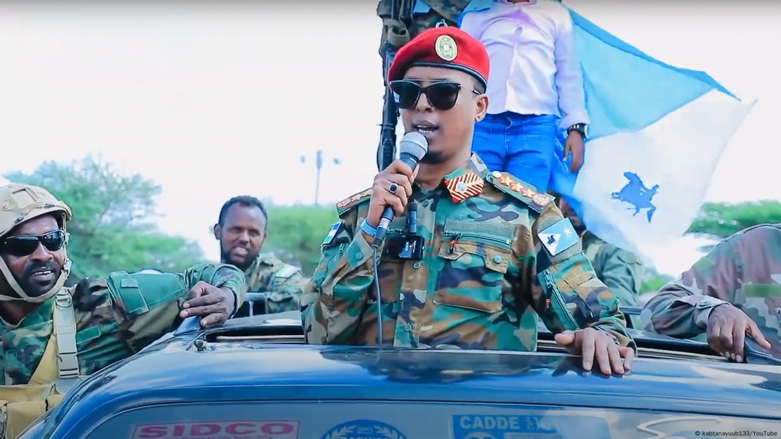 Ayub Abdirizak in a car's moonroof, wearing sunglasses and a microphone and talking to supporters