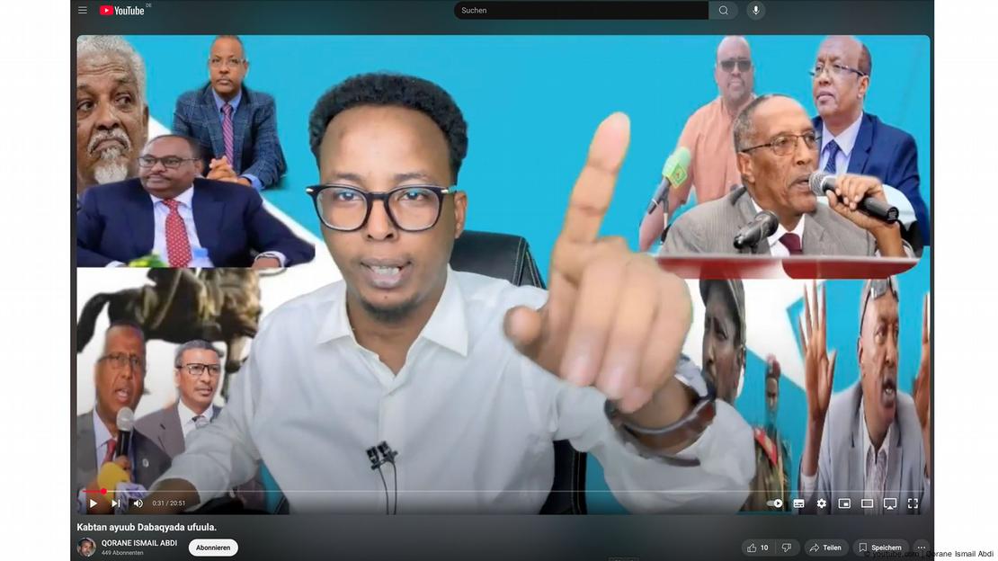 Ayub Abdirizak sitting in front of a picture wall with a raised finger