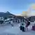 People stand with their luggage as smoke billows from a wildfire, in Ferma, on the island of Crete, Greece, July 2, 2025 in this still image from video obtained from social media