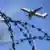 A photo of a plane transporting detainees as seen departing from behind razorwire