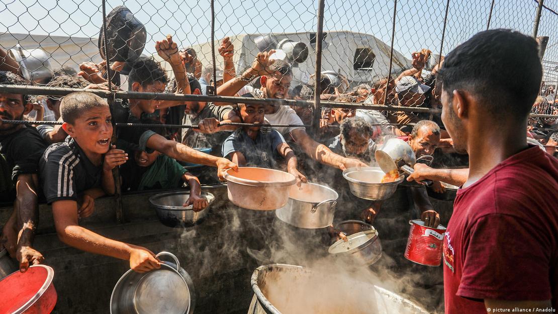 Distribución de alimentos en Jan Yunis: niños y adultos extienden sus manos con recipientes tratando de recibir comida.