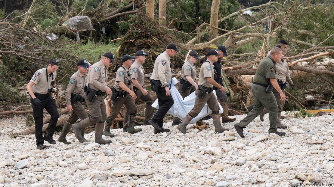Guardabosques de Texas y fuerzas del orden locales trasladan el cuerpo de una víctima de la inundación desde las orillas del río Guadalupe durante las operaciones de recuperación el 5 de julio de 2025 cerca de Hunt, Texas, pasando junto áboles caídos.