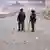 Riot police with head protection and sticks stand on a road littered with rocks in front of smoke during demonstrations in the Kangemi slum of Nairobi, Kenya