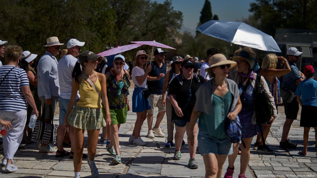 Pessoas caminham com sombrinhas sob o sol em dia de calor extremo na Grécia