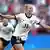 jugadora de fútbol festeja con brazos abiertos en la cancha tras convertir gol.