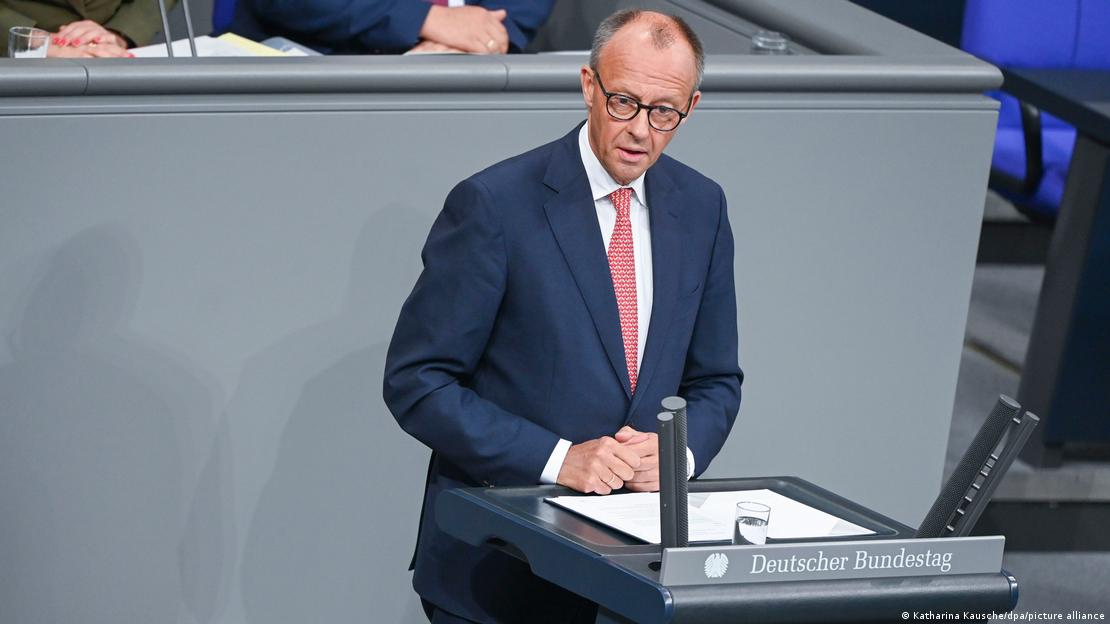 Deutschland Berlin 2025 | Bundeskanzler Friedrich Merz steht in der Generaldebatte zum Haushalt im Bundestag am Rednerpult. Er trägt einen dunkelblauen Anzug, weißes Hemd und eine rot-weiße Krawatte