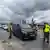 Das Bild zeigt Grenzkontrollen am Grenzübergang in Slubice, Polen, zu Deutschland. Polnische Grenzschützer kontrollieren einen schwarzen Mercedesbus. Im Hintergrund sind Flaggen der EU sowie ein Transparent mit der Aufschrift "Stop Imigracji" zu sehen