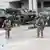 Vier Nationalgardisten mit Gewehren im Anschlag und mehrere Militärfahrzeuge vor einem Gebäude