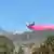 El avión, volando a baja altura, descarga agua tintada de rojo sobre una zona boscosa humeante, el pasado 10 de julio, seis días después de iniciarse el incendio.