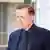 Ein jüngerer Mann (Adis Ahmetovic) in einem dunklen Anzug, spricht zu einem nicht sichtbaren Gesprächspartner