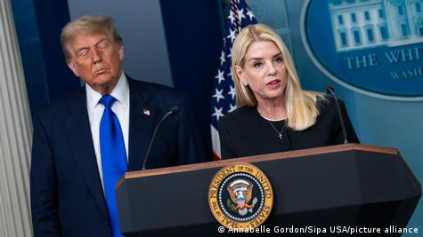 ABD Adalet Bakanı Pam Bondi bir basın toplantısında kürsüde gazetecilerin sorularına yanıt veriyor, arkasında da Başkan Donald Trump duruyor