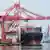 Shipping containers are being loaded onto a cargo ship at the Jakarta International Container Terminal (JICT) in Tanjung Priok Port