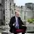 Kanzler Merz sitzt beim ARD-Sommerinterview unter freiem Himmel. Im Hintergrund sieht man das Reichstagsgebäude.