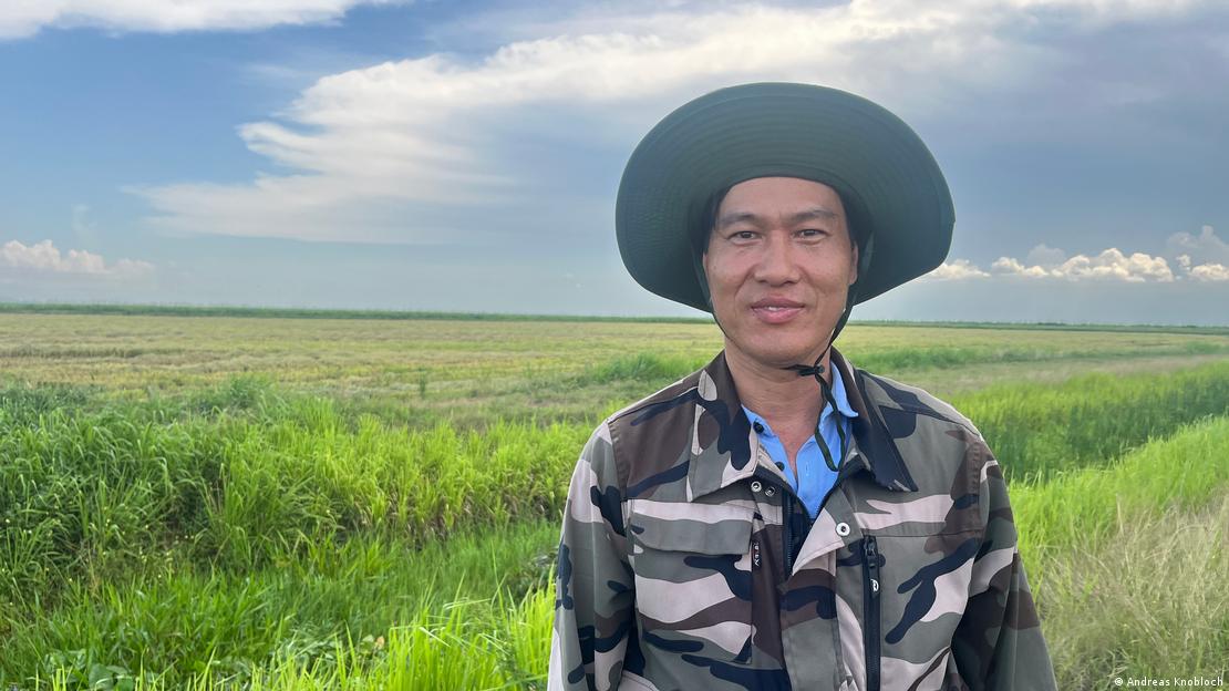 Un hombre con un sombrero y un campo de arroz detrás.