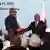 Two men (Sumbu Sita Mambu of the DRC [l.] and M23 Executive Secretary Benjamin Mbonimpa [r.]) hold leather-binders as they shake hands while looking into the camera in Qatar on July 19, 2025 