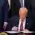 Beyaz Saray'daki makamında bir belge imzalayan ABD Başkanı Donald Trump ve arkasında duran takım elbiseli kişiler