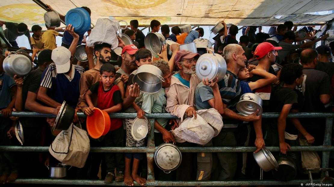 Viele Menschen mit Schüsseln und Kochtöpfen an einer Absperrung 