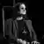 Osbourne sits on a velvet chair on stage, smiling