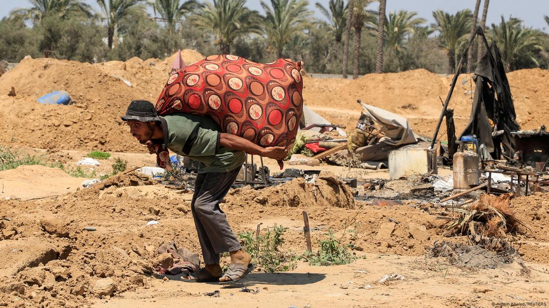 Un hombre camina llevando sobre sus espaldas sus pertenencias en un paisaje de desolación y destrucción. Un hombre camina llevando sobre sus espaldas sus pertenencias en un paisaje de desolación y destrucción.