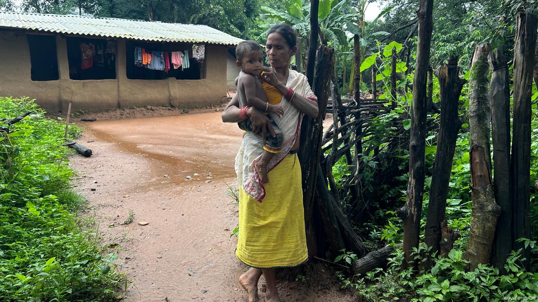 Sukli Oyam carrying the daughter of her son Ramesh in front of her house