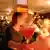 A woman speaking to a man holds a red cocktail at a bar