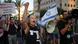 En la imagen se muestra a una manifestante gritando a través de un megáfono y al fondo un grupo de personas con carteles y una bandera de Israel. En la imagen se muestra a una manifestante gritando a través de un megáfono y al fondo un grupo de personas con carteles y una bandera de Israel.