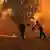 Firefights attemp to throw water as a fire rages on the ground in a forest